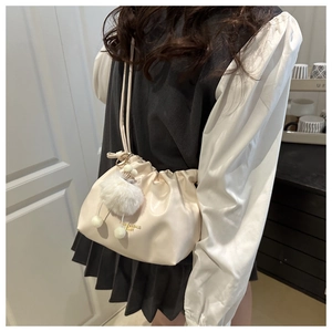 Detail view of cream cloud bag with gold lettering, shoulder strap and plush pompom charm
