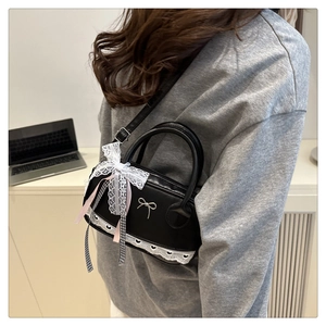 Detail of black crossbody bag with white lace bow and elegant silver ribbon hardware