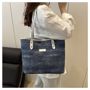 Détail du sac cabas en denim bleu avec étiquette en cuir blanc et rivets argentés