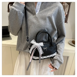 Detail of black cross-body bag with metal bow decoration and white heart lace trim
