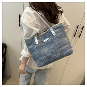 Detail of blue denim tote bag with silver chain strap and metal rivet accents
