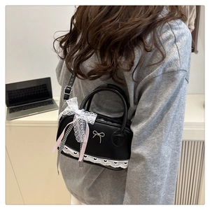 Detail of black crossbody bag featuring white lace trim and decorative ribbon bow