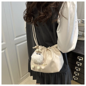 Detail of cream pleated crossbody bag featuring a soft faux fur pompom and drawstring