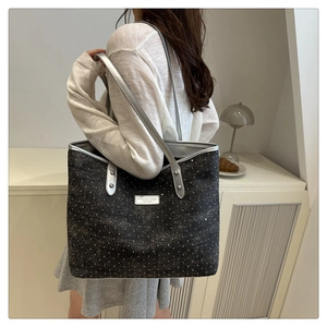 Detail of a sparkling black sequin tote bag with a silver shoulder strap and logo plaque