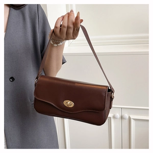 Detail einer tiefbraunen Baguette-Tasche mit goldenem Drehverschluss auf glänzendem Leder