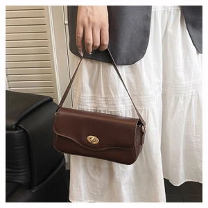 Detail of a brown leather underarm bag featuring a golden metallic twist-lock closure