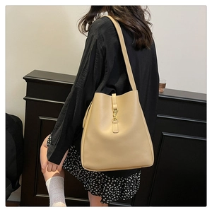 Side view of beige leather bucket bag with gold lock buckle worn by a female model