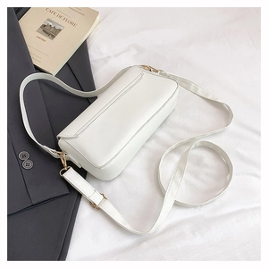 Close-up of white leather handbag with adjustable gold metal buckle on white fabric