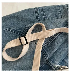 Détail du tissu denim bleu avec bandoulière en velours côtelé blanc et boucle