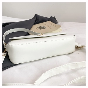 Close-up of white leather crossbody bag with golden metal twist lock and fine texture