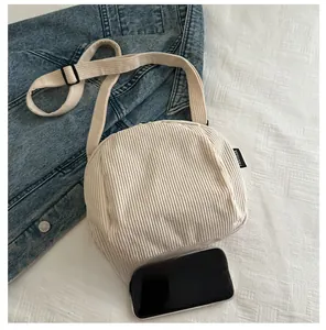 Détail de la texture d'un sac bandoulière en velours côtelé crème avec un téléphone portable