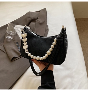 Detail of black textured crescent bag featuring white pearls and silver heart charms