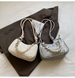 Detail of white and silver underarm bags with heart charms and pearl chain accents
