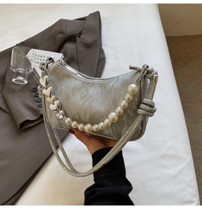 Close-up of silver crescent bag featuring elegant pearl and heart-shaped metal chain strap