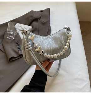Detail of silver metallic hobo bag featuring pearl strap and heart pendant detail