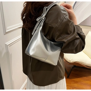 Detail shot of a silver metallic hobo bag featuring a large decorative bow on the shoulder strap