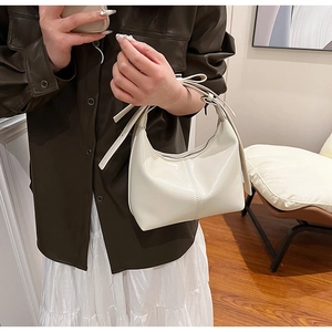 Détail d'un sac hobo blanc en cuir verni avec nœud décoratif et finition brillante