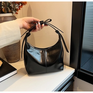 Detail of black glossy hobo bag featuring a top handle with a decorative bow knot