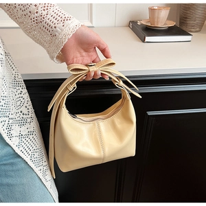 Detail of cream bucket bag showing elegant bow decoration and textured faux leather finish
