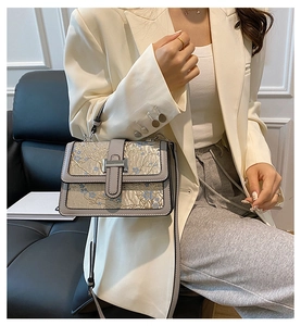 Detail of floral embroidery on light gray crossbody bag carried by a model