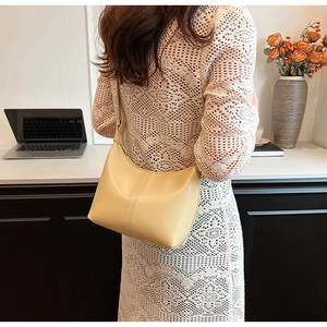 Minimalist cream leather half-moon baguette bag worn by a model in a bright office setting