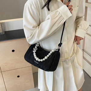 Minimalist black pleated underarm bag with pearl heart chain worn by model in soft light
