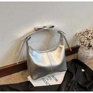 Détail d'un sac à bandoulière argenté avec nœud décoratif posé sur un livre blanc