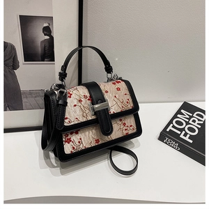 Detail of floral embroidery on beige handbag with black leather trim and silver clasp