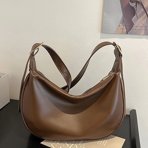 Brown PU leather crescent shoulder bag with gold hardware in a modern minimalist setting