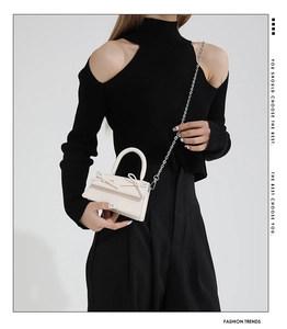 Detail of mini crossbody bag with delicate bows and silver chain strap on cream leather
