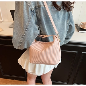 Détail du sac bandoulière plissé rose montrant la texture et les ferrures dorées sur modèle