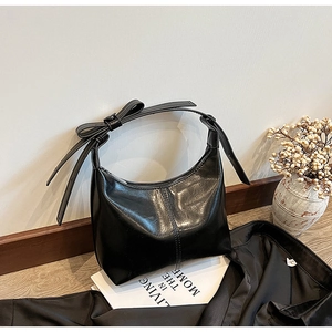 Vue détaillée du sac croissant en cuir noir brillant avec un nœud papillon sur la bandoulière