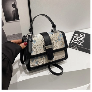 Close-up of beige jacquard handbag with blue floral embroidery and black leather trim