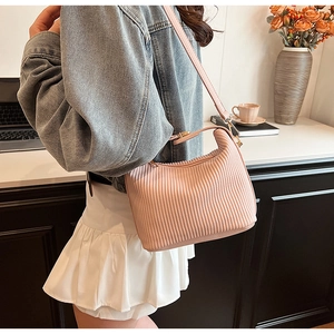 Sac bandoulière plissé rose avec ferrures dorées porté par un mannequin sur une jupe blanche et jean