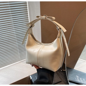 Détail d'un sac à bandoulière crème avec nœud décoratif et silhouette en demi-lune