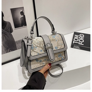 Detail of grey PU leather crossbody bag featuring intricate blue floral embroidery