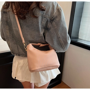 Détail d'un sac bandoulière rose plissé avec finitions dorées porté par un mannequin