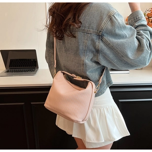 Détail du sac bandoulière plissé rose avec fermeture éclair dorée sur un bureau