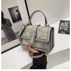 Close-up of elegant floral embroidery and satin texture on a gray crossbody handbag