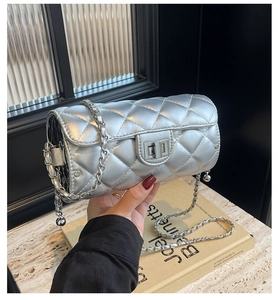 Détail d'un sac cylindrique argenté matelassé avec fermoir rotatif et bandoulière chaîne