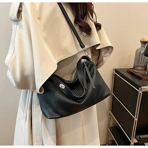 Detail view of black pleated texture hobo bag with silver clasp on beige trench coat