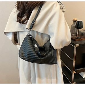 Detail of black pleated texture bag with silver buckle worn over a beige coat
