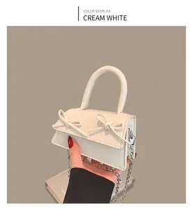 Detail of cream mini crossbody bag featuring dual ribbon bows and metallic chain strap
