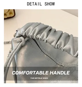 Détail du sac à main argenté avec poignée plissée, motifs floraux et anneaux en métal