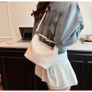Détail du sac bandoulière blanc plissé avec sangle et boucles métalliques sur un bureau