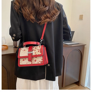 Close-up of floral embroidery on a red textured leather crossbody bag with metal buckle