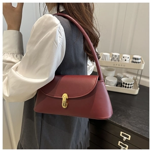 Detail of burgundy leather shoulder bag with gold metal clasp on a stylish model