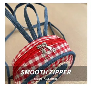 Detail view of smooth metal zippers on a red checkered canvas and denim backpack