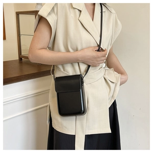 Close-up of a minimalist black leather crossbody phone bag on a model in a lifestyle setting
