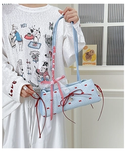 Detail of light blue shoulder bag featuring red bow patterns and lace ribbon handle